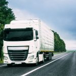 White prime mover driving on highway with green trees and blue sky